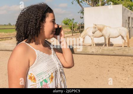 Focused woman listening to her phone near beautiful horses Stock Photo