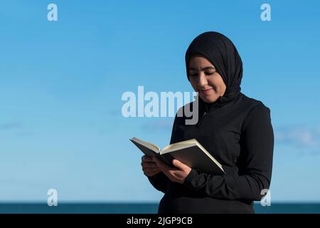 Muslim woman with a hijab reading a book outdoors. Stock Photo
