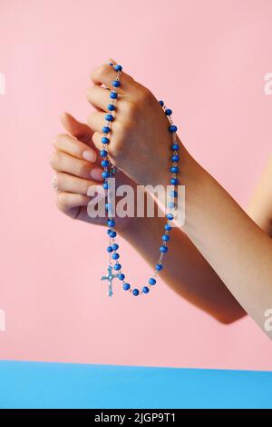 closeup hands with rosary praying in front of pink background Stock Photo