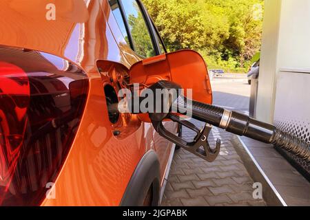 Fill car with fuel in petrol station. Pumping gasoline fuel in orange car at a gas station. Close up. Stock Photo