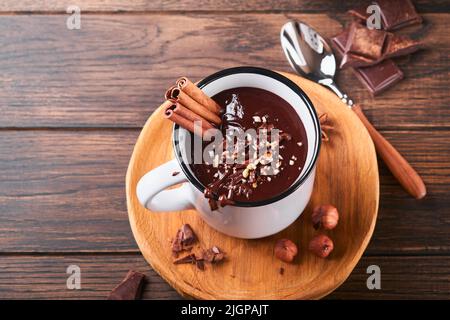 Hot chocolate. Homemade spicy hot chocolate with cinnamon, crushed hazelnut in enamel mug on old wooden background. Cozy seasonal holidays. Stock Photo