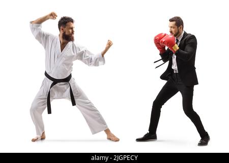 Full length profile shot of a businessman with boxing gloves fighting with a man in karate kimono isolated on white background Stock Photo