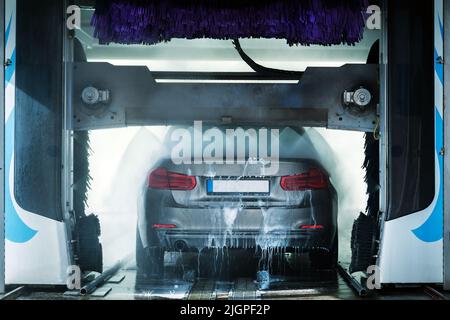 A grey business sedan vehicle running through an automatic car wash with brushes and water hitting car. Stock Photo