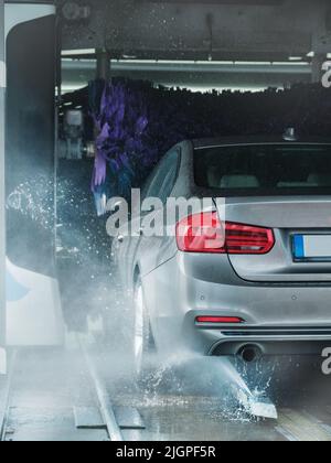 A grey business sedan vehicle running through an automatic car wash with brushes and water hitting car. Stock Photo