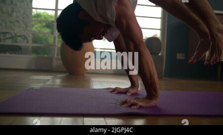 Man doing difficult Yoga handstand posture at home. Athletic person practices workout at living room on mat Stock Photo