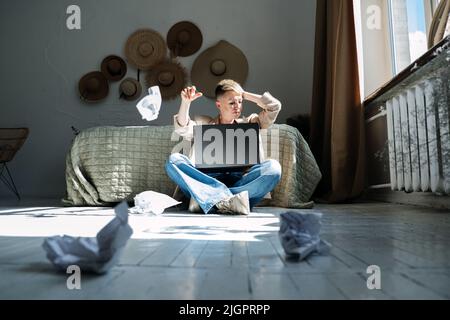 Woman professional content writer working with papers and laptop computer at home while sitting on the floor. Stock Photo