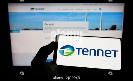Person holding cellphone with logo of power transmission company Tennet Holding BV on screen in front of business webpage. Focus on phone display. Stock Photo