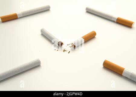 Broken cigarette in half with orange filter against the background of whole cigarettes. Isolated on white background. Smoking is harmful. Healthy lifestyle concept. Close-up square photo. Stock Photo