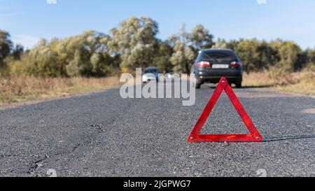 Emergency triangle stands on the road in front of cars on the background. Breakdown of the car in sunny weather. Safety of the road traffic Stock Photo