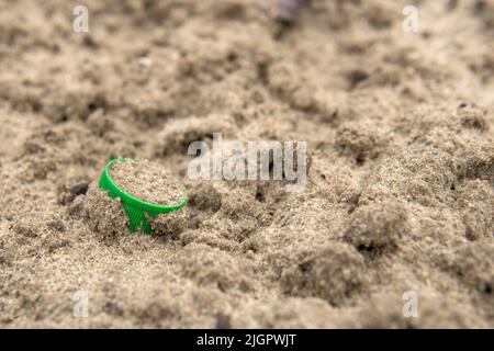 A green cork from a plastic bottle lies in the sand. Environmental pollution with plastic waste. Nature protection concept. Save ecology for future generations. Stock Photo