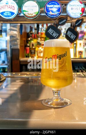 A just poured full pint of San Miguel lager or beer with a frothy head in a San Miguel branded glass on the bar counter of a JD Wetherspoons pub