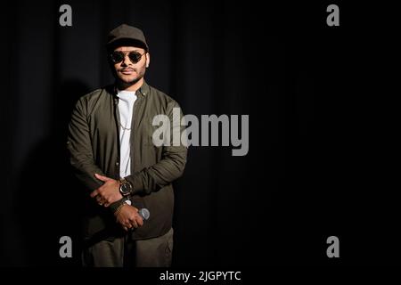 eastern hip hop performer in sunglasses holding microphone on black Stock Photo