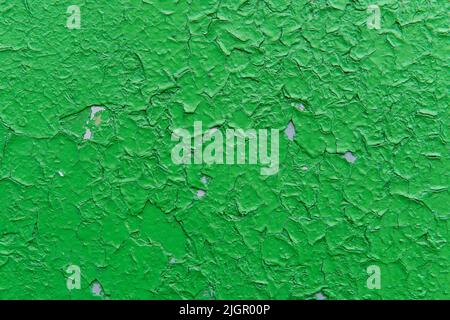 Old green colored cracked paint, that applied to an old gray wall. Grunge wall texture for design. Old paint texture. Colored cracked abstract background.  Stock Photo