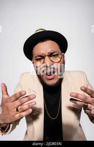 eastern hip hop performer in eyeglasses singing while gesturing isolated on grey Stock Photo