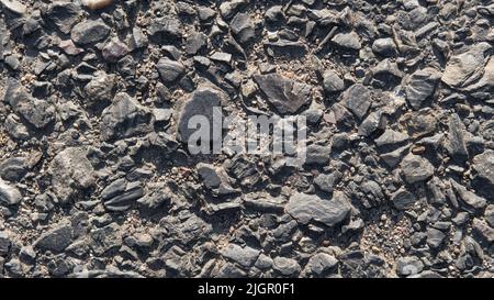 Old crashed road. Black pebbles background. Natural stone. Close-up texture of pebbles. Stones in the asphalt ground  Stock Photo