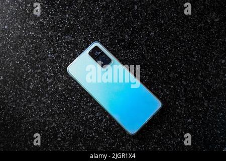 A blue sparkling mobile phone with four cameras on a black surface. Trendy color device. Stock Photo