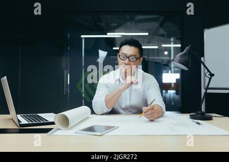 Thinking asian engineer architect working in modern design office, man looking at drawing plan. Stock Photo