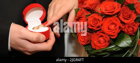 Marriage proposal male hands offer a box with a ring a woman touches it gently with a finger on the side lies a red huge bouquet Box Red woman has red manicure Boxes lie rings, it is open Stock Photo