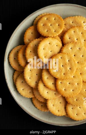 Salty Round Crackers on a Plate on a black surface, top view. Flat lay, overhead, from above. Stock Photo