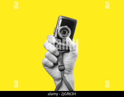 Man hand holding point and shoot camera. Black and white image on yellow background. Practical and compact digital device for taking photos in photographer arm. Stock Photo