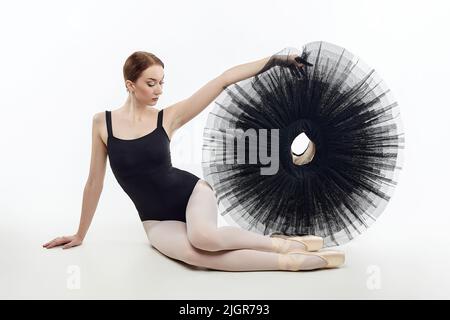 attractive ballerina sits and holds a tutu in her hands. studio photo shoot on a white background. Stock Photo