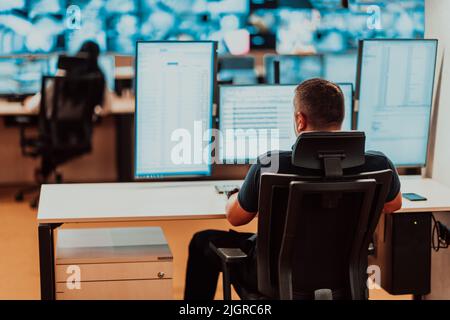 Male security operator working in a data system control room offices Technical Operator Working at workstation with multiple displays, security guard Stock Photo