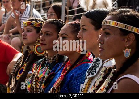 Kahnawake, Canada. 10th July, 2022. Pow-wow dancers wearing traditional costumes watch the presentation. The 30th Annual Echoes of a Proud Nation pow-wow brought in thousands of people from all across North America to celebrate Native people culture and traditions in the Mohawk Reserve of Kahnawake. After a two-year hiatus, the biggest pow-wow in Quebec offered a time to meet, dance, sing, visit and celebrate with friends and family. Credit: SOPA Images Limited/Alamy Live News Stock Photo