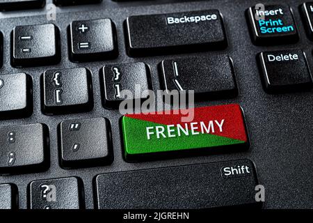 Frenemy word on the green red enter key of a computer keyboard. Laptop enter key with warning message. Be an enemy while pretend to be a friend. Stock Photo