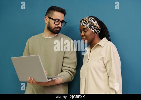 Two young employees looking for online information and discussing it while preparing presentation of their new business project Stock Photo