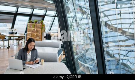Young Asian business woman wearing suit working in big office using phone. Stock Photo