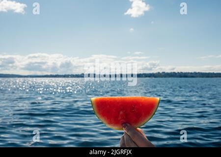 hand holding up watermelon semi moon, circle slice out on boat, lake Stock Photo