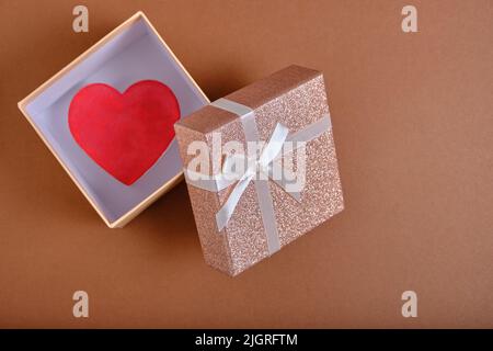 Open gift box with heart inside brown background is tied with beige ribbon with bow Stock Photo