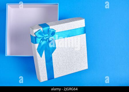Open gift box with blue ribbon and bow blue background Stock Photo