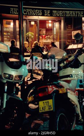 Their motorcycles parked at the curb, diners eat on he sidewalk outside a cafe in the Montmartre district of Paris, France. Stock Photo