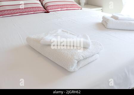 White folded towels on a hotel bed with white sheets. Stock Photo