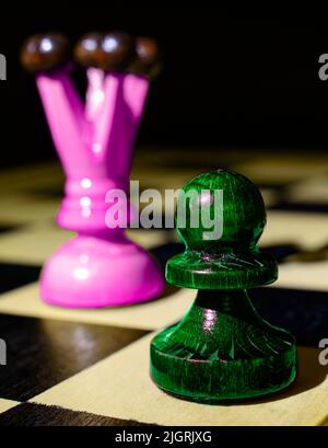 Green pawn and purple Queen on a chessboard. Dark background. Selective focus. Abstract chess composition. Macro photo. Stock Photo