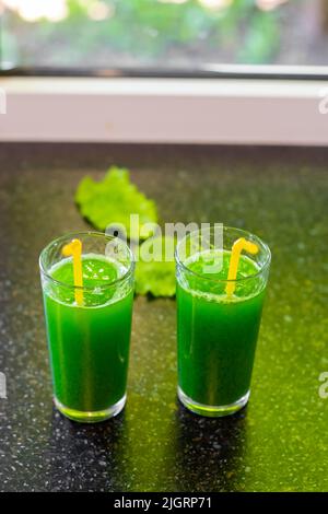 A green drink made from fresh vegetable greens with chlorophyll in glasses on the countertop, against the background of the window. Stock Photo