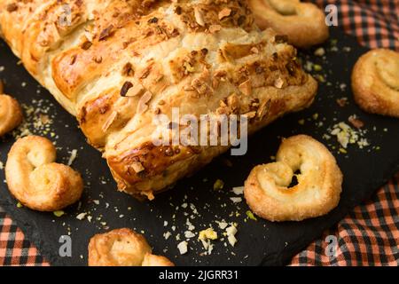 Image of a puff pastry filled with chocolate or cocoa cream next to artisan puff pastry palm trees, all on a black slate plate Stock Photo