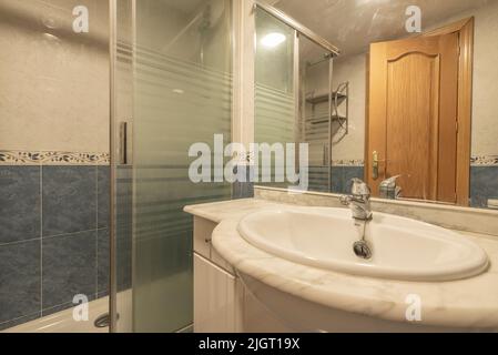 Small vacation home bathroom with quarter turn shower stall, wall mirror and half wall blue tiled porcelain sink Stock Photo