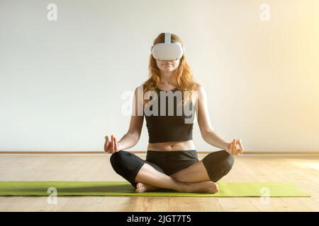 A young woman in virtual reality glasses makes yoga asana. Future technology concept. Stock Photo