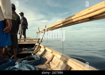 Whale hunters scouting around to find a sign of whale as they are standing on traditional whaling boat that is sailing on Savu Sea off the coast of Lamalera in Wulandoni, Lembata, East Nusa Tenggara, Indonesia. Stock Photo