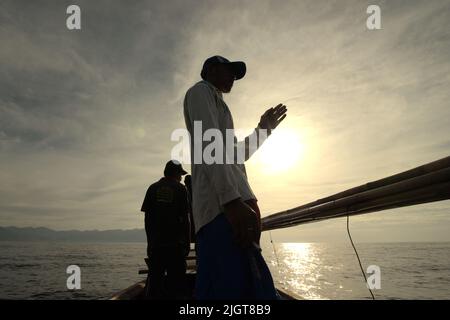 Whale hunters scouting around to find a sign of whale as they are standing on traditional whaling boat that is sailing on Savu Sea off the coast of Lamalera in Wulandoni, Lembata, East Nusa Tenggara, Indonesia. Stock Photo