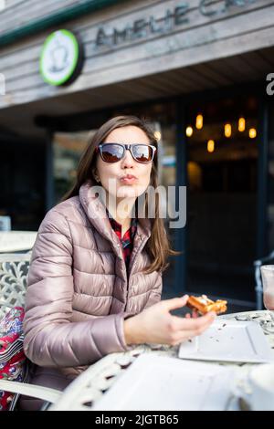 A woman in a cafe eats waffles for dessert and sends out an air kiss. Vertical photo. Stock Photo