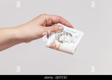 Stack of ten pound notes of the Bank of England in female hand. Close-up photo over gray wall background Stock Photo