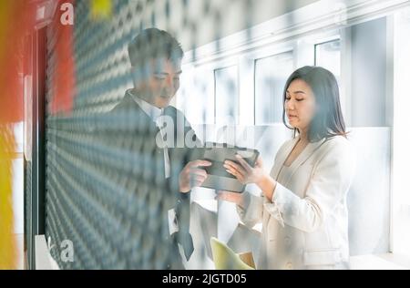 Two business colleagues talking to each other while looking at a digital tablet. Modern office setting. Stock Photo