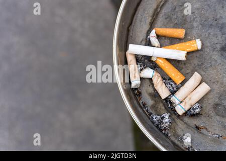 burned eyeball with cigarette Close up top bird eye view metal ashtray with burned out stubbed out smoked  cigarettes with orange filters and copy space as concept for unhealthy lif  Stock Photo