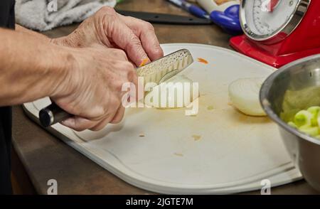 Chef cuts the onion into slices on the board in the home kitchen Stock Photo