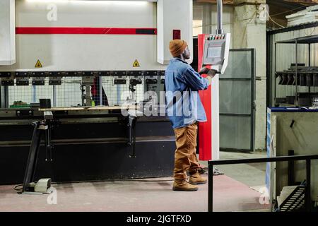 African worker in workwear standing in front of computer and choosing the program on machine before starting the work Stock Photo