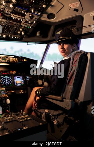 Portrait of female aviator sitting in airplane cabin to fly aircraft, pushing dashboard command buttons and power switch. Flying plane with control panel lever and radar navigation windscreen. Stock Photo