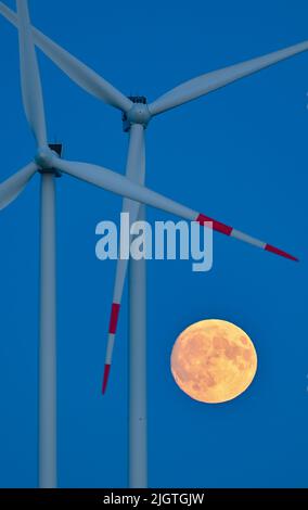 Sieversdorf, Germany. 12th July, 2022. The moon, which is about 95 percent visible and waxing, glows yellowish in the sky next to wind turbines shortly after sunset. On the night of July 13, 2022, a super full moon can be seen in the sky if visibility is good. At moonrise around 10 p.m., the Earth's satellite will be 357,517 kilometers from Earth. Despite this distance, it will be the largest supermoon of the year. Credit: Patrick Pleul/dpa/Ģ����ý Live News Stock Photo